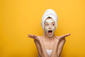 shocked girl with nourishing facial mask showing shrug gesture on yellow background