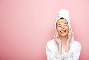 happy girl with citrus facial mask touching face with closed eyes isolated on pink