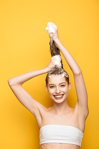 happy girl  while washing long hair on yellow background