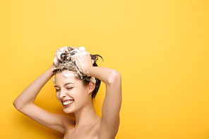 cheerful girl with closed eyes washing hair on yellow background