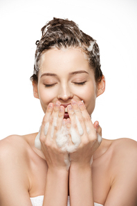 cheerful girl with closed eyes covering mouth with hand while washing hair isolated on white