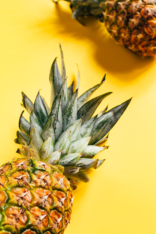 selective focus of fresh ripe pineapples with green leaves on yellow background
