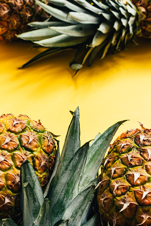 selective focus of fresh ripe pineapples with green leaves on yellow background