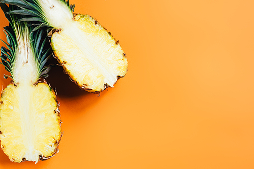 top view of cut ripe pineapple with green leaves on orange background