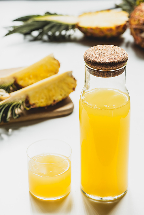 selective focus of fresh pineapple juice in bottle and glass near cut delicious fruit on cutting board on white background
