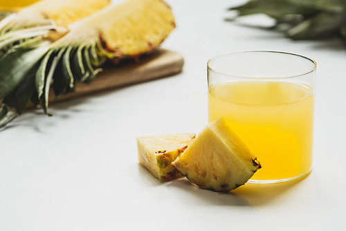 selective focus of fresh pineapple juice near cut delicious fruit on cutting board on white background