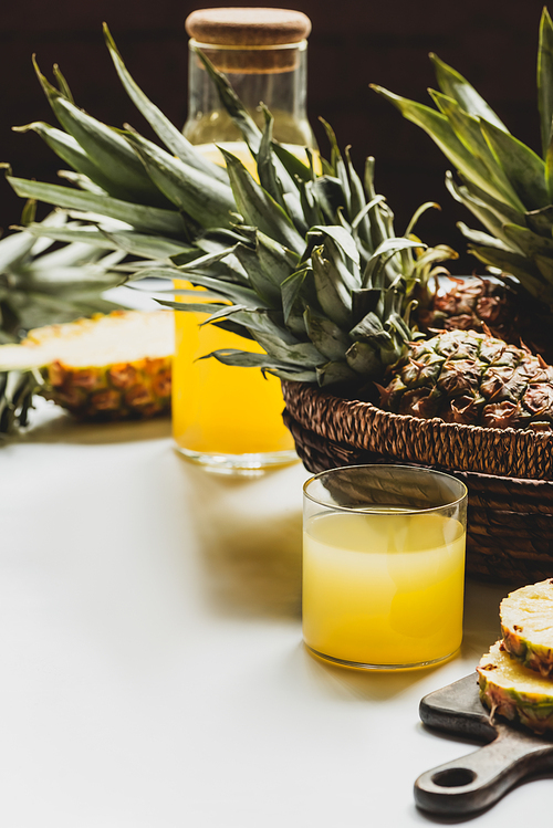 selective focus of fresh pineapple juice in glass and bottle near delicious fruit in basket on white surface isolated on black