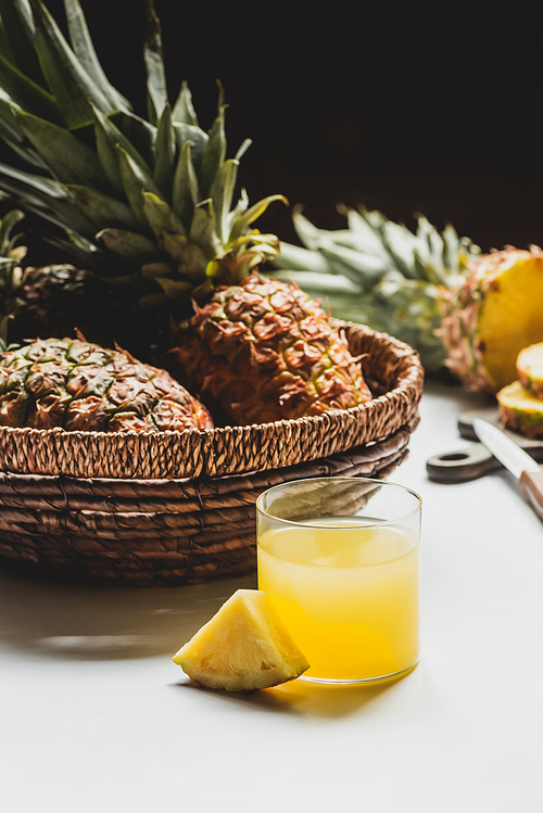 selective focus of fresh pineapple juice in glass near delicious fruit in basket on white background isolated on black