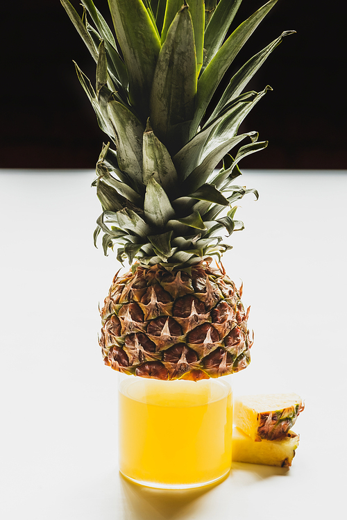 fresh pineapple juice in glass near cut delicious fruit on white surface isolated on black