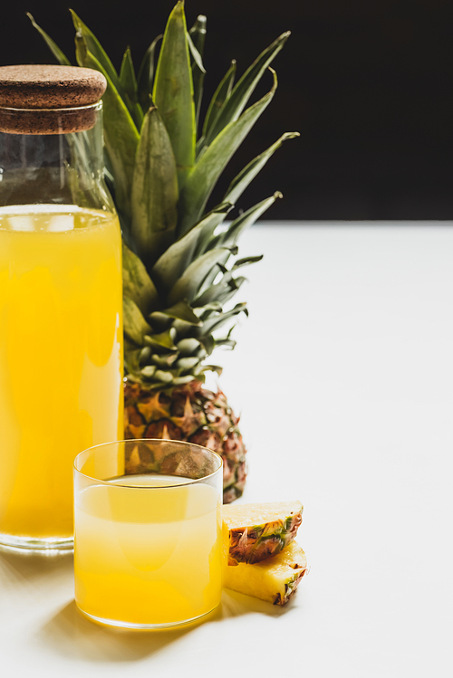 fresh pineapple juice in bottle and glass near cut delicious fruit on white surface isolated on black