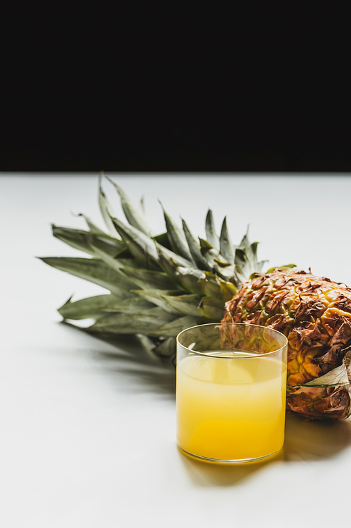 fresh pineapple juice near cut delicious fruit on white surface isolated on black