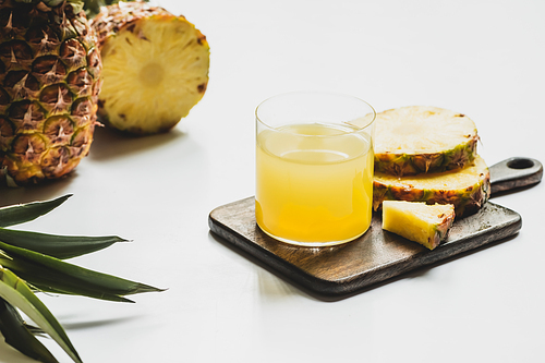 fresh pineapple juice in glass near cut delicious fruit on wooden cutting board on white background