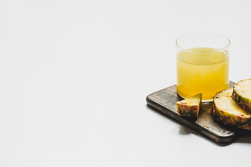 fresh pineapple juice in glass near cut delicious fruit on wooden cutting board on white background