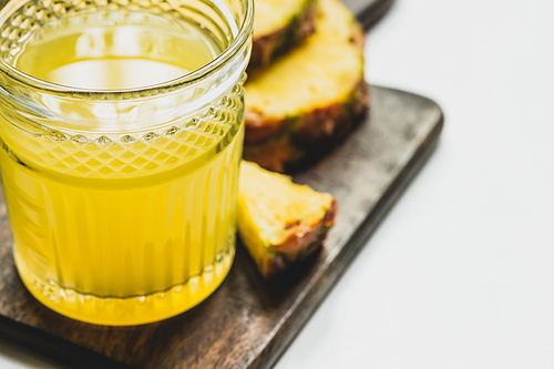 selective focus of fresh pineapple juice in glass near cut delicious fruit on wooden cutting board on white background