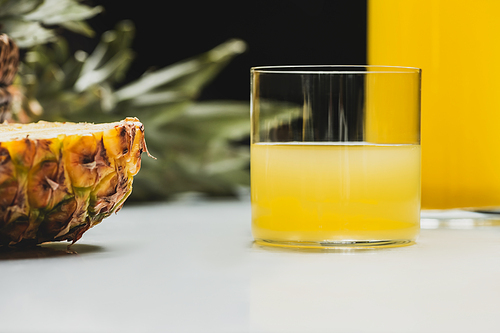 selective focus of fresh pineapple juice and cut delicious fruit on white surface on black background