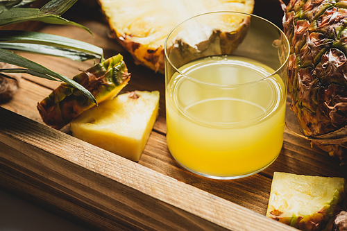 close up view of fresh pineapple juice and cut delicious fruit on wooden tray