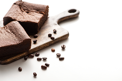 selective focus of delicious brownie pieces on wooden cutting board with coffee beans on white background