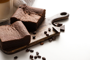 delicious brownie pieces on wooden cutting board with coffee beans and chocolate on white background