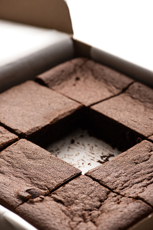 close up view of delicious brownie pieces in cardboard box on white background