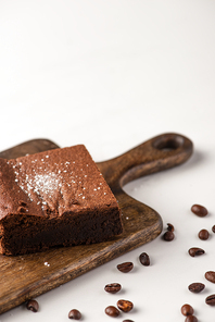 delicious brownie piece on wooden cutting board with coffee beans on white background