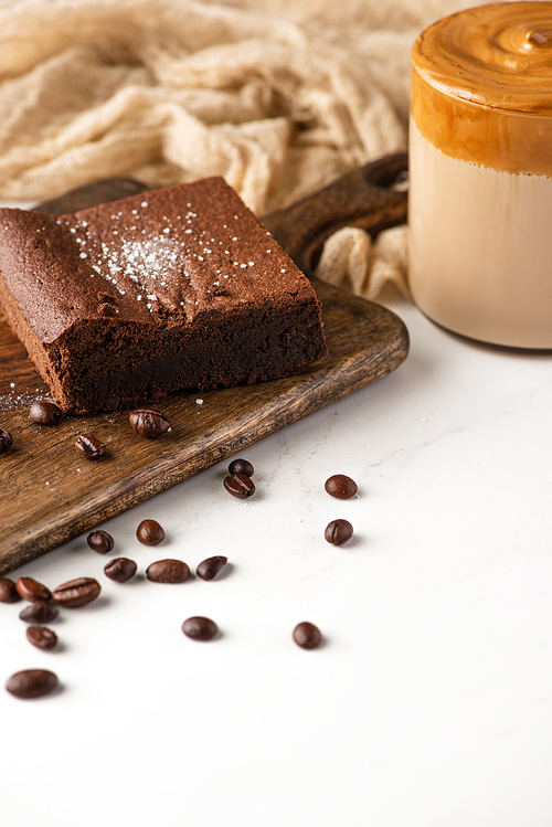 delicious brownie piece on wooden cutting board with coffee beans, coffee and cloth on white background