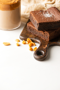 selective focus of delicious brownie pieces on wooden cutting board with peanuts near coffee in glass on white background