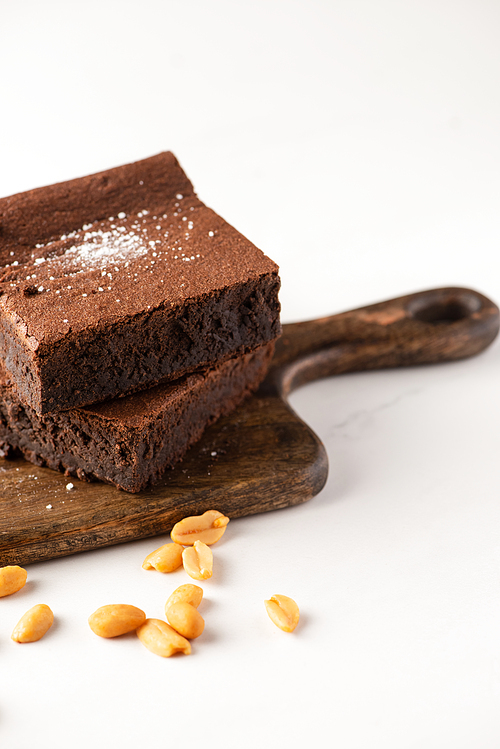 delicious brownie pieces on wooden cutting board with peanuts on white background