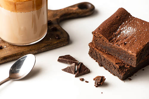 delicious brownie pieces near wooden cutting board with coffee and spoon on white background