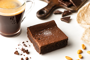 selective focus of delicious brownie piece near coffee on white background
