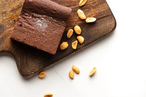 top view of delicious brownie piece on wooden cutting board with nuts on white background
