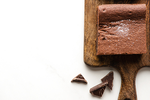 top view of delicious brownie piece on wooden cutting board with chocolate on white background