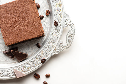 top view of delicious brownie piece with coffee beans and chocolate on silver tray on white background