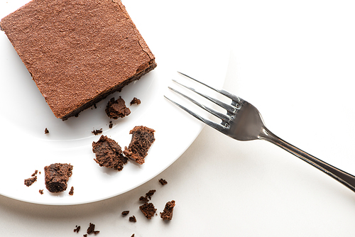 top view of delicious brownie piece on plate with fork on white background