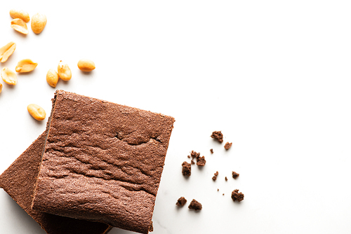top view of delicious brownie pieces and peanuts on white background