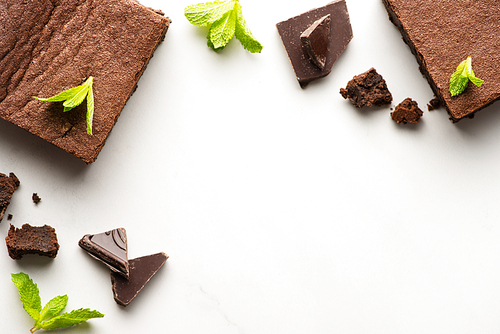 top view of delicious brownie pieces with mint and chocolate on white background