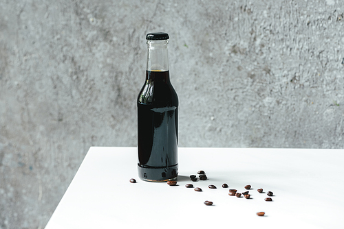 cold brew coffee in bottle near coffee beans on white table