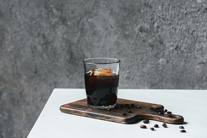 cold brew coffee with ice in glass and coffee beans on chopping board on white table