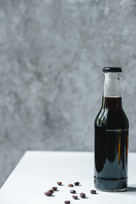 cold brew coffee in bottle near coffee beans on white table