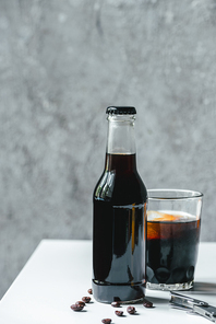 cold brew coffee with ice in glass and bottle near coffee beans and opener on white table