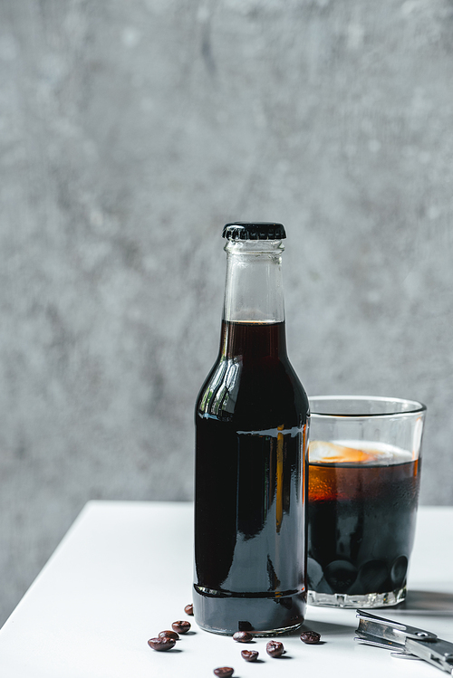 cold brew coffee with ice in glass and bottle near coffee beans and opener on white table
