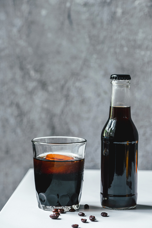 cold brew coffee with ice in glass and bottle near coffee beans on white table
