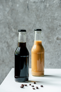 selective focus of cold brew coffee in bottles near coffee beans on white table