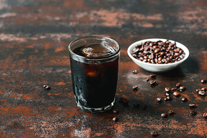 selective focus of cold brew coffee with ice in glass near coffee beans on rusty surface