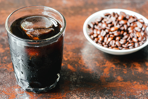 selective focus of cold brew coffee with ice in glass and bottle near coffee beans on rusty surface