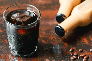 selective focus of cold brew coffee with ice in glass and bottle near coffee beans on rusty surface