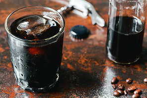 selective focus of cold brew coffee with ice in glass and bottle near coffee beans on rusty surface