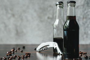 selective focus of cold brew coffee in bottles near opener and coffee beans