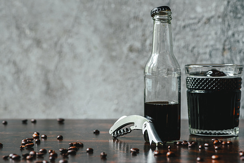 cold brew coffee in glass and bottle near opener and coffee beans