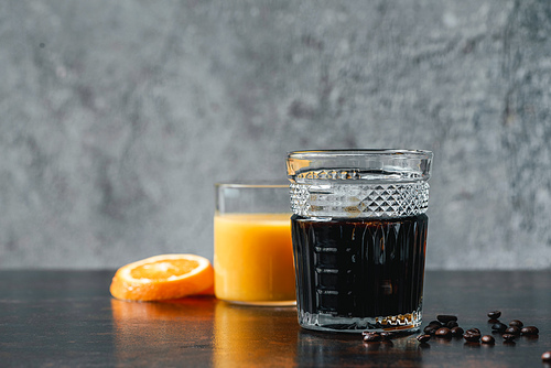 selective focus of cold brew coffee in glass near orange juice and coffee beans