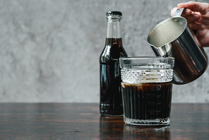 cropped view of woman adding milk to cold brew coffee in glass near bottle